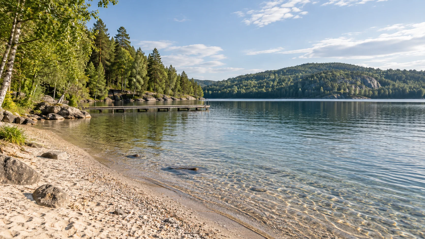 Rolig innsjø med sandstrand, skog og en liten badebrygge.